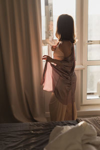 Young woman wearing sunglasses while sitting on bed at home