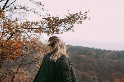 Rear view of woman standing by tree against clear sky