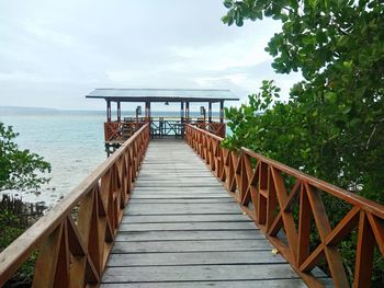 Empty long wooden jetty leading to sea against sky