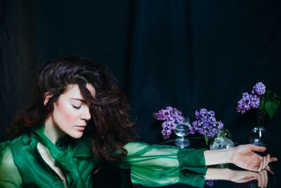 Woman by flowers in vase on table against black background