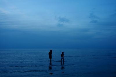 Silhouette friends standing in sea against sky at dusk