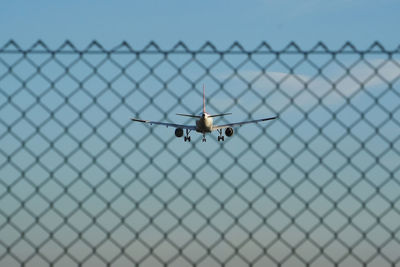 Close-up of airplane on chainlink fence against clear blue sky