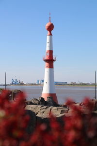 Lighthouse by sea against clear blue sky