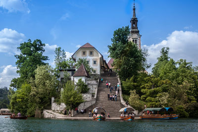 People by boats on building by trees against sky