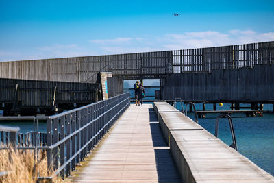 Man walking on footbridge against sky