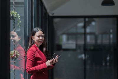 Young woman using phone while standing on laptop
