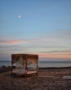 Lifeguard chair on beach against sky at sunset