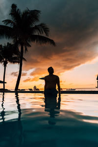 Silhouette man standing by swimming pool against sky during sunset