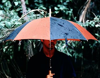 Man holding umbrella while standing against plants during rainy season