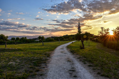 Road amidst field against sky during sunset