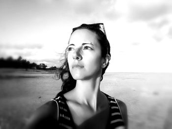 Thoughtful woman standing at beach against sky