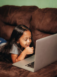 Cute girl using laptop while lying on sofa at home