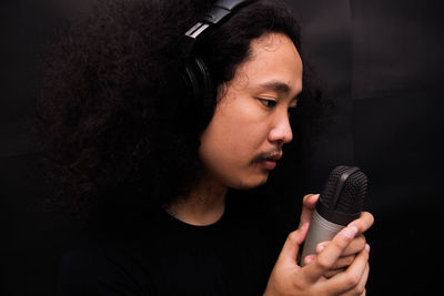 Close-up of young singer holding microphone against black background