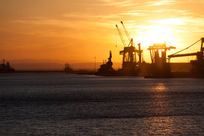 Silhouette of cranes at harbor during sunset