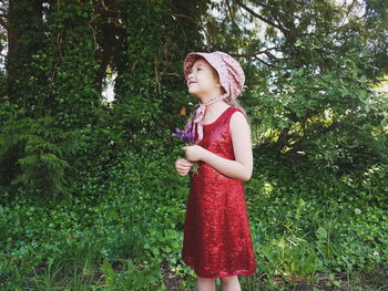 Girl in red dress looking away while standing against trees