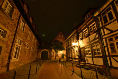 Illuminated street amidst buildings against sky at night