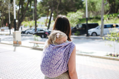 Side view of woman carrying baby on back standing on street