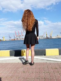 Rear view of woman standing by sea against sky