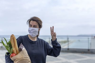 Portrait of woman wearing mask holding food against sky