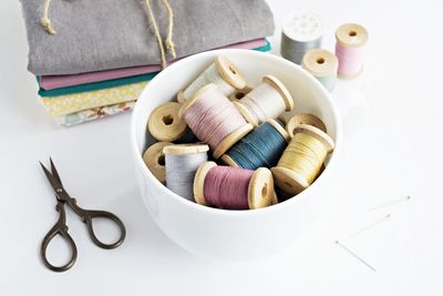 High angle view of thread spools in mug by textiles on table