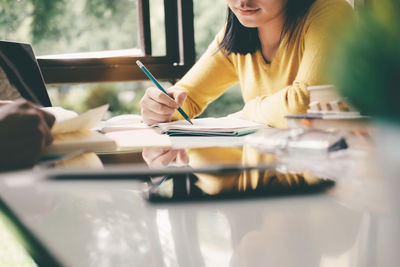 Midsection of woman reading book while sitting at table