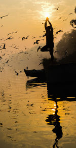 Silhouette man on boat in lake against sky during sunset