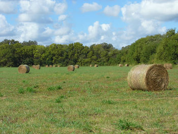 Hay bales on field against cloudy sky