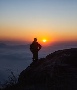 Silhouette man standing on rock against sky during sunset