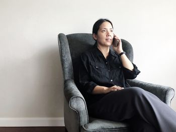 Young woman sitting on sofa against wall