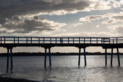 Silhouette bridge over sea against sky