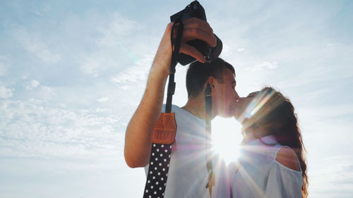 Young couple kissing on mouth against sky during sunny day