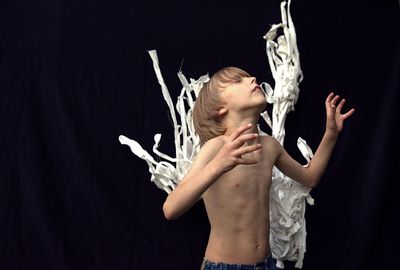 Shirtless boy with fabric standing against black background