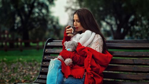 Young woman having drink while sitting on bench in park