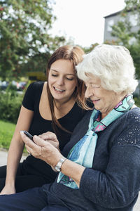 Young woman looking at grandmother using smart phone at park
