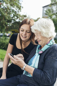 Woman holding mobile phone while sitting on man using laptop