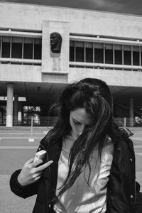 Young woman using mobile phone while standing against built structure