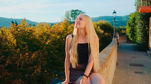 Young woman sitting on plant against trees