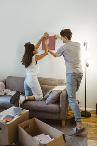 Couple helping each other while mounting photo frame on wall at home