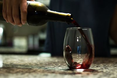 Close-up of hand pouring drink in glass on table