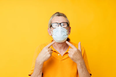 Portrait of young woman holding face against yellow background