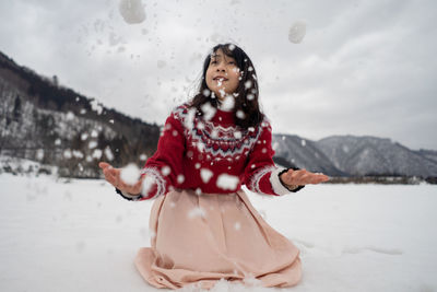 Smiling woman playing while kneeling on snow