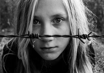 Close-up portrait of girl by barbed wire