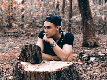 Young woman looking away while sitting on tree trunk in forest