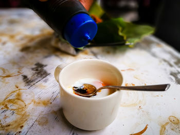 Half boiled eggs with soy sauce and pepper served in a cup on a stained table.