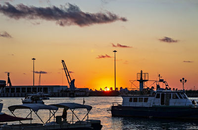 Orange sunset on sea in port with floating yachts and palm trees in distance against setting sun