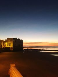 Buildings by sea against sky at sunset