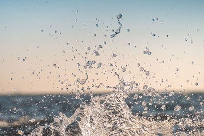 Close-up of water splashing on window against sky