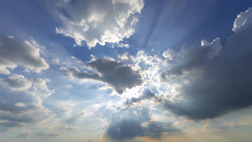 Low angle view of sunlight streaming through clouds