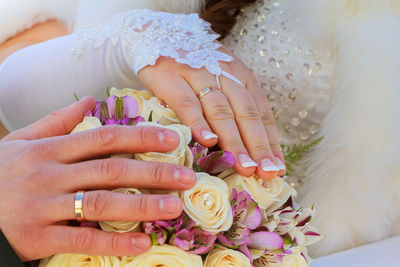 Cropped hand of groom with bride touching bouquet during wedding