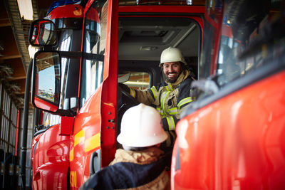 Smiling firefighter talking to coworker while sitting in fire truck at fire station